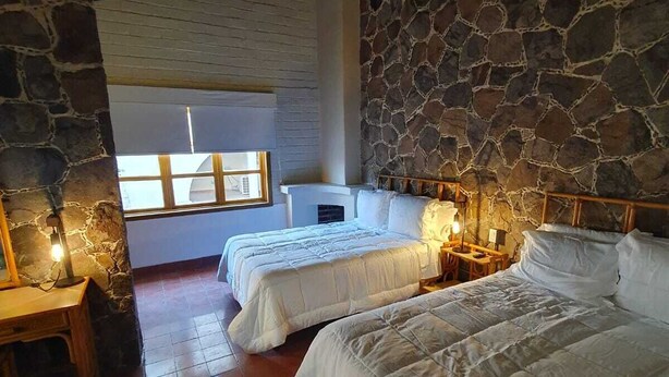 A room with two beds, stone walls, a wooden ceiling, and a large window.