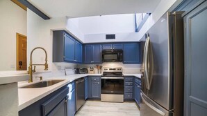 Een moderne keuken met blauwe kastjes, roestvrijstalen apparatuur en een dakraam.