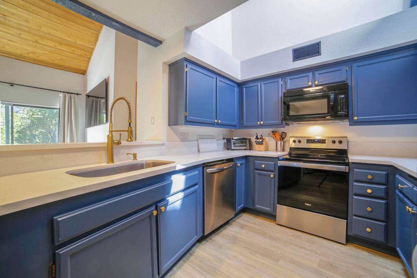 A modern kitchen with blue cabinets, stainless steel appliances, and a large window.