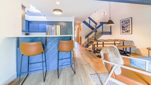 Een moderne keuken met blauwe kasten, een bar met twee krukken, een eethoek met een tafel en stoelen, en een trap met blauwe accenten.