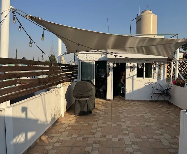 A patio with a covered seating area, a grill, and a water tank in the background.