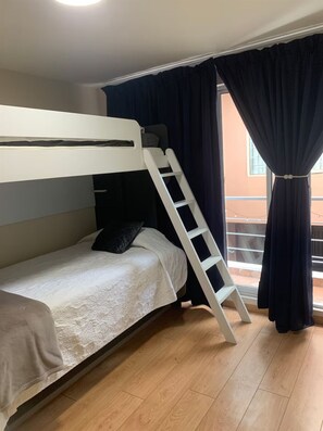 A bunk bed with a ladder, a window with curtains, and a wooden floor.