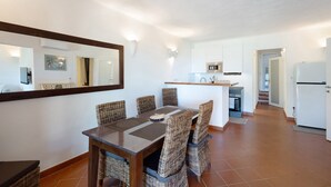 A dining area with wicker chairs, a wooden table, and a kitchen in the background.