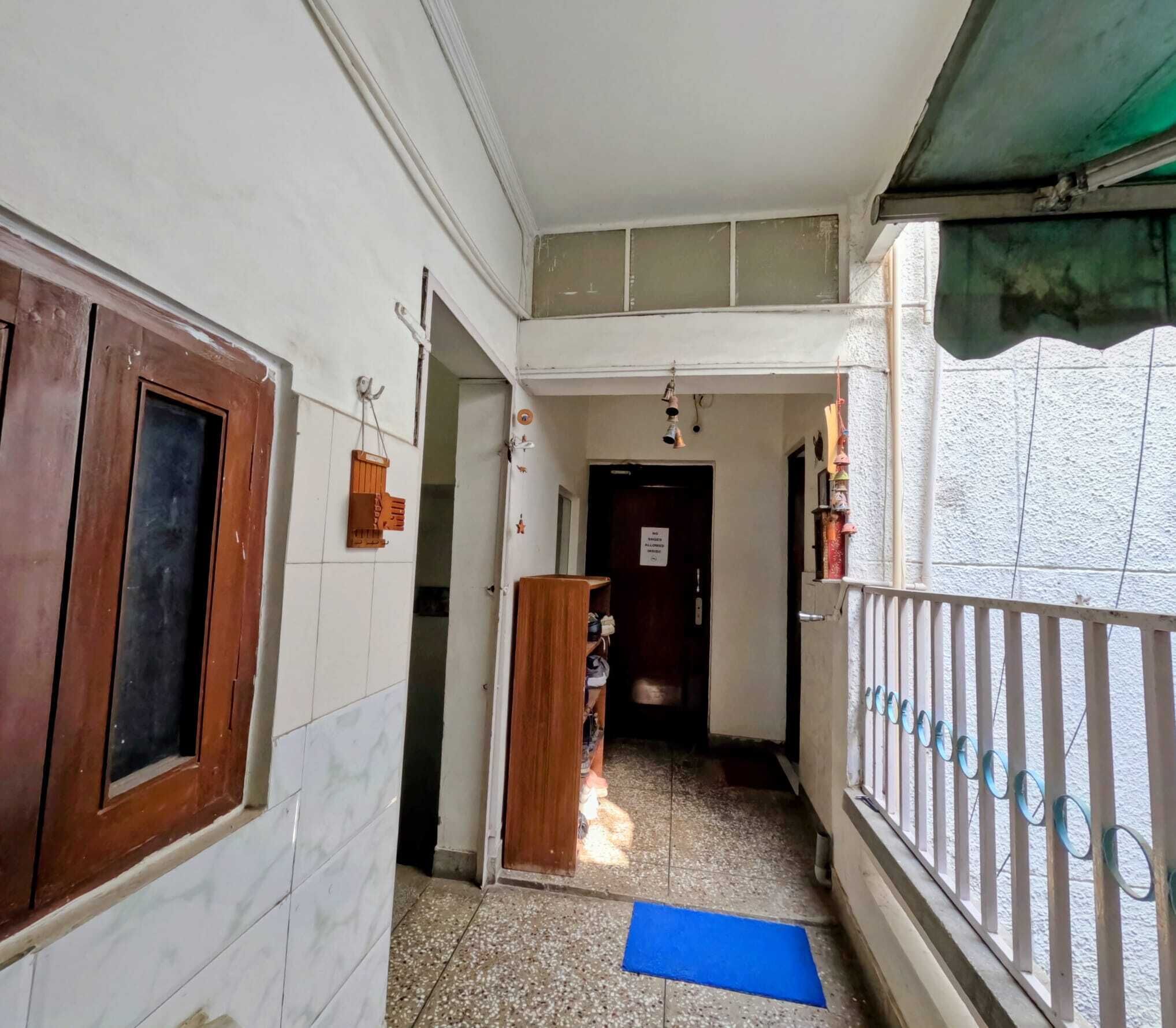 A narrow corridor with a wooden door on the left, a blue mat on the floor, and a metal railing on the right.