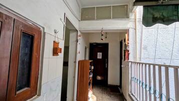 A narrow corridor with a wooden door on the left, a blue mat on the floor, and a metal railing on the right.