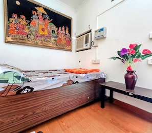 A room with a bed, a wall-mounted air conditioner, a painting, and a vase with flowers. - Gavari India's Delhi Hostel (New Delhi)