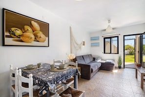 A dining area with a table set for four, a gray sofa, and a painting of fruit on the wall.