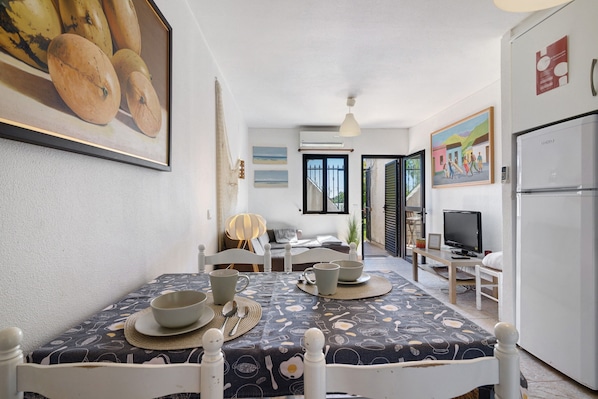 A dining area with a table set for four, a television, and a refrigerator in the background.