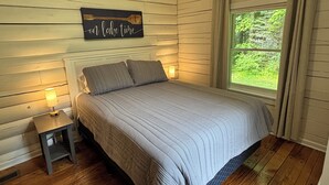 A bedroom with a bed, nightstands, a window with curtains, and a wall-mounted sign.