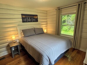 A bedroom with a bed, nightstands, a window with curtains, and a wall-mounted sign.