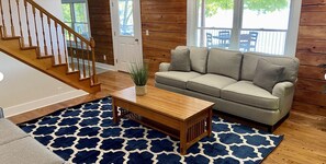 Ein Wohnzimmer mit einer Holztreppe, einem beigefarbenen Sofa, einem Holztisch und einem gemusterten Teppich.