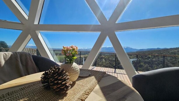 A room with a large window, a wooden table, a vase with flowers, and a pine cone.