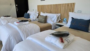 A hotel room with two beds, each with white linens and pillows, a wooden headboard, a bedside table with a lamp, and a small nightstand.