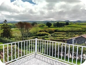 Un balcone con ringhiera bianca che si affaccia su un paesaggio verde con alberi e campi.