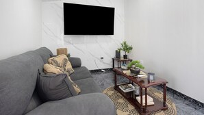 A modern living room with a grey sofa, a flat-screen TV mounted on the wall, a wooden side table with a plant, and a marble floor. - Holiday Home 'Casa Do Pacheco' with Sea View, Wi-Fi and Air Conditioning (Salga)