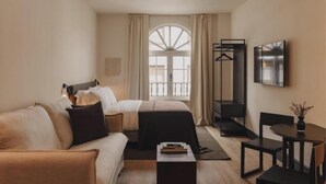 A hotel room with a bed, a sofa, a desk, a chair, a TV, and a window with curtains. - Copla Bilbao (Bilbao)