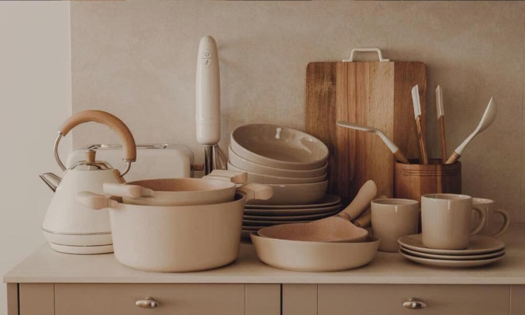 A kitchen with various utensils and cookware, including a kettle, pots, and a wooden cutting board.