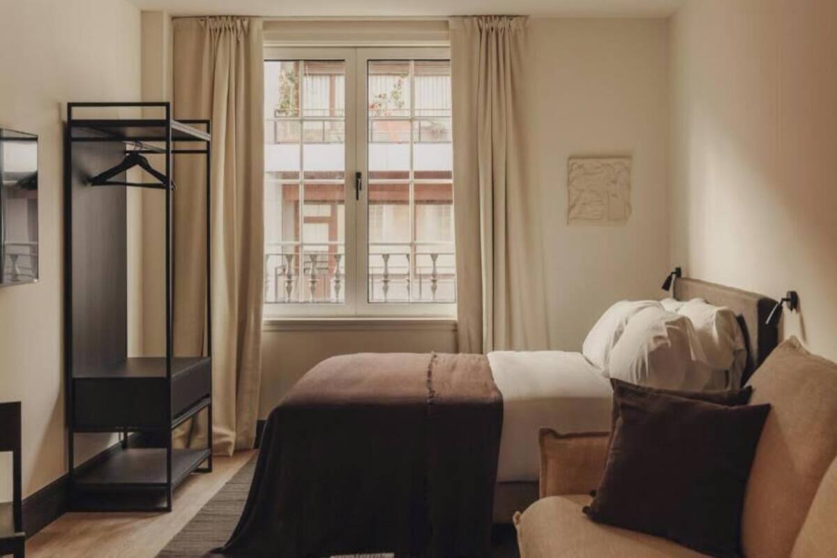 A hotel room with a bed, a sofa, a wardrobe, and a window with curtains.