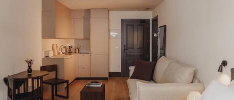 Un espacio habitable compacto con kitchenette, comedor y zona de estar con sofá y mesa de centro.