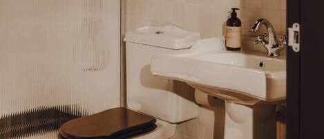 Un baño con inodoro, lavamanos y una botella de jabón para manos.