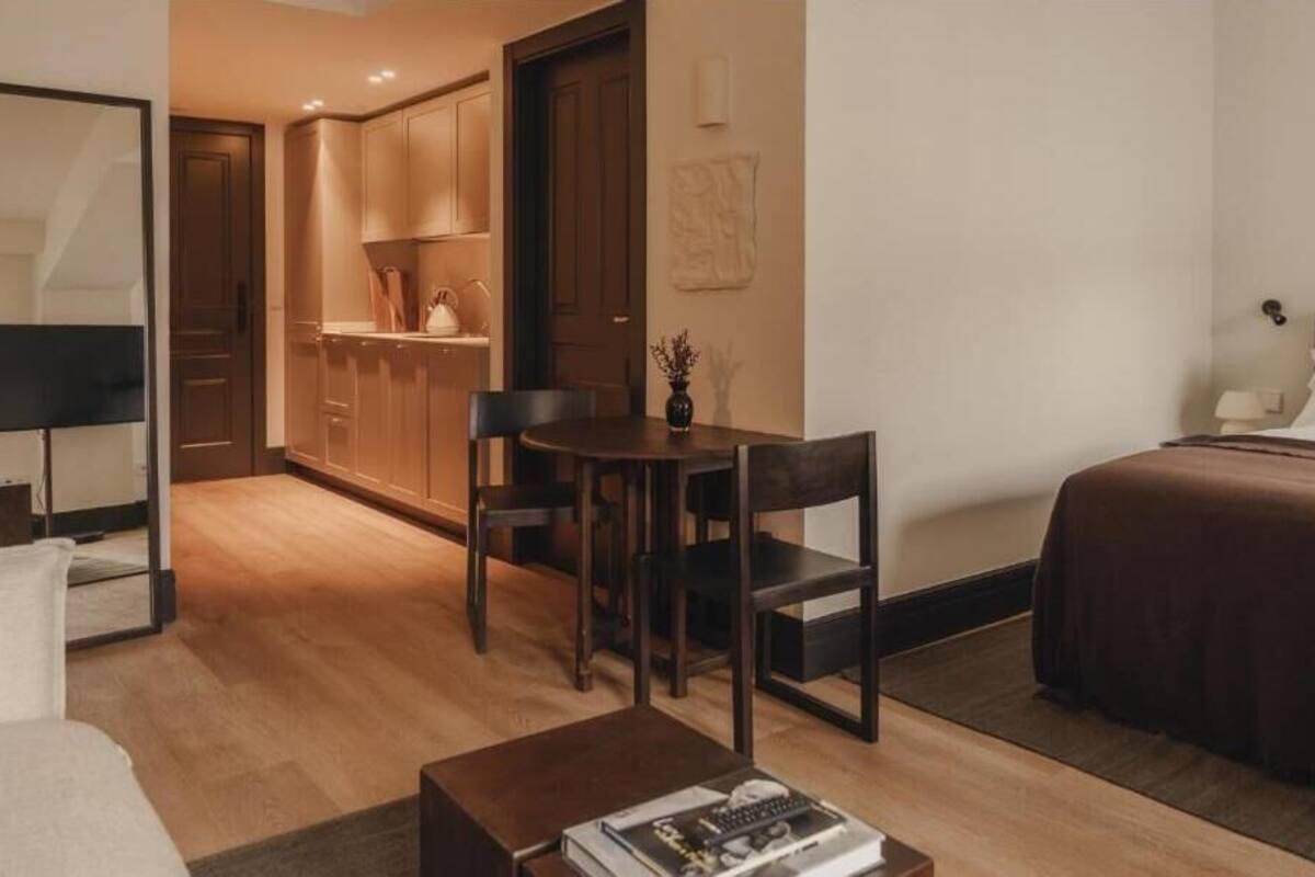 A compact hotel room with a bed, a small dining table with chairs, a sofa, a coffee table, and a kitchenette area.