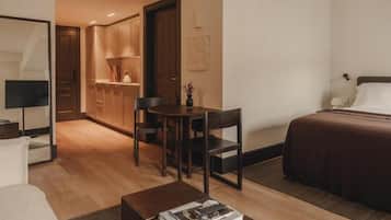 A compact hotel room with a bed, a small dining table with chairs, a sofa, a coffee table, and a kitchenette area.
