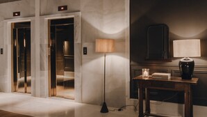 An elevator with a digital display, a floor lamp, a table with a vase, and a book. - Copla Bilbao (Bilbao)