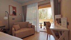 A hotel room with a sofa, a dining table with chairs, a lamp, and a view of the outdoors. - Ionian Crown Suites in Barbati  (Corfu)