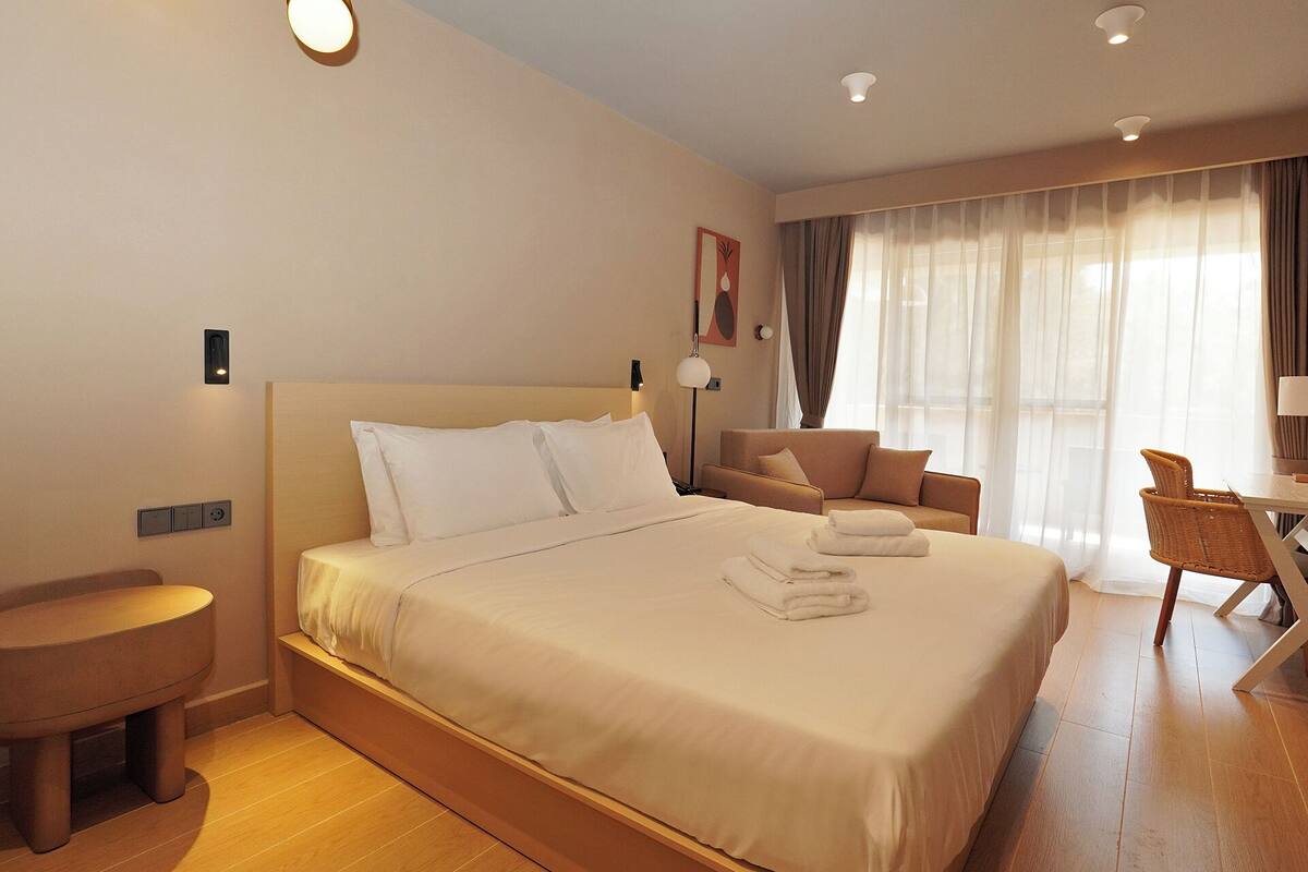 A hotel room with a large bed, a seating area with a chair, a small table, and a window with curtains.