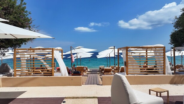A beachside lounge with wooden structures and white umbrellas, overlooking a clear blue sea. - Ionian Crown Suites in Barbati  (Corfu)