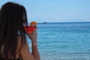 Une personne tenant un verre, avec la mer en toile de fond et un bateau visible au loin.