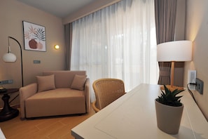 A modern living room with a sofa, a wicker chair, a dining table, a potted plant, a lamp, and a wall-mounted power outlet.