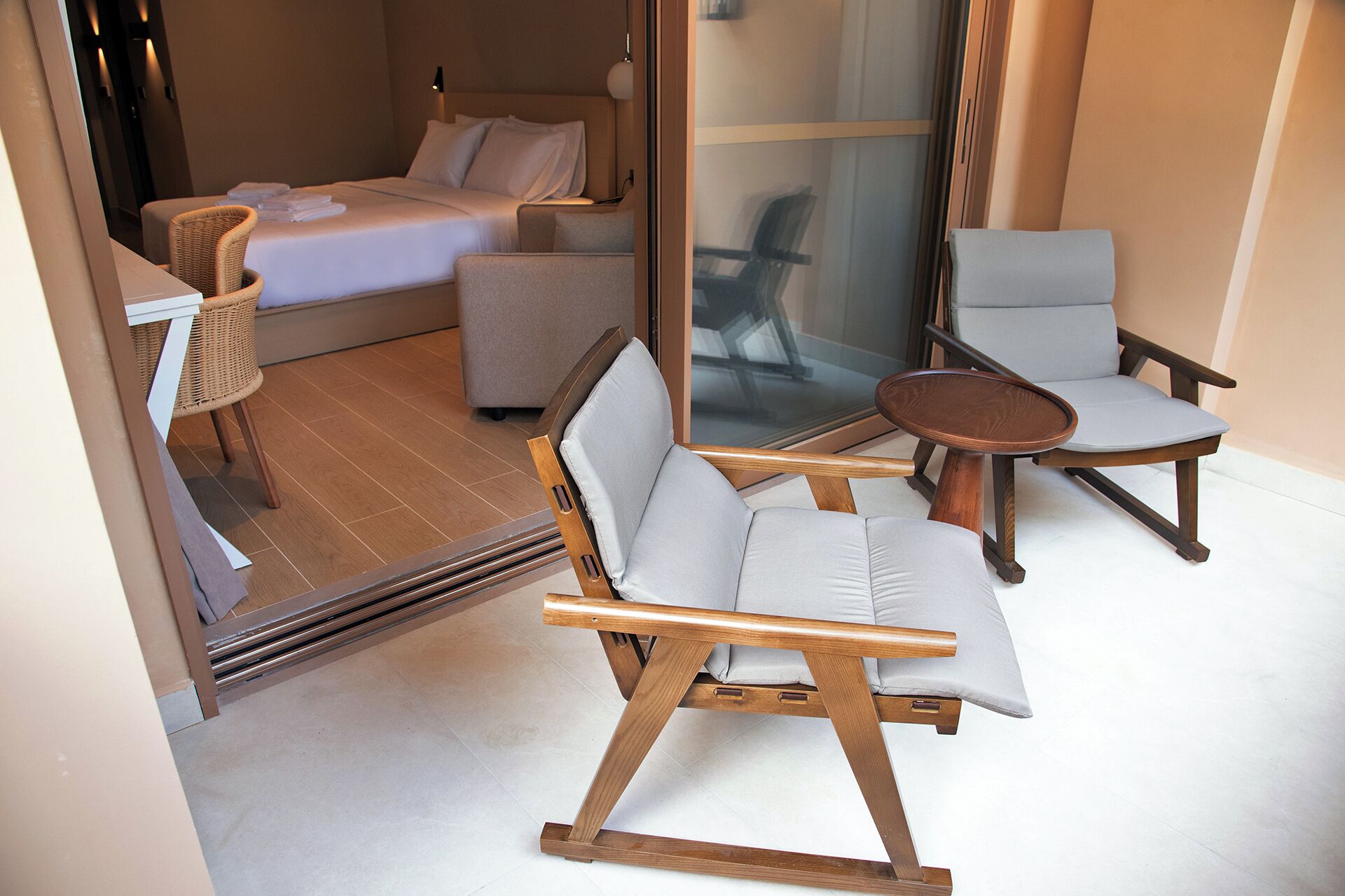 A compact room with a bed, two chairs, a small table, and a wicker chair.