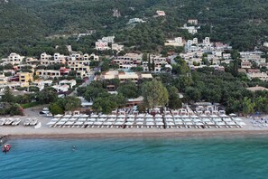 Vue aérienne d’une ville côtière avec ses bâtiments, une plage avec des transats et un quai pour bateaux.
