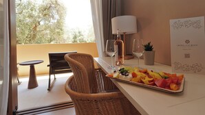 A dining area with a wicker chair, a table with a fruit platter, wine glasses, a bottle, and a menu. - Ionian Crown Suites in Barbati  (Corfu)