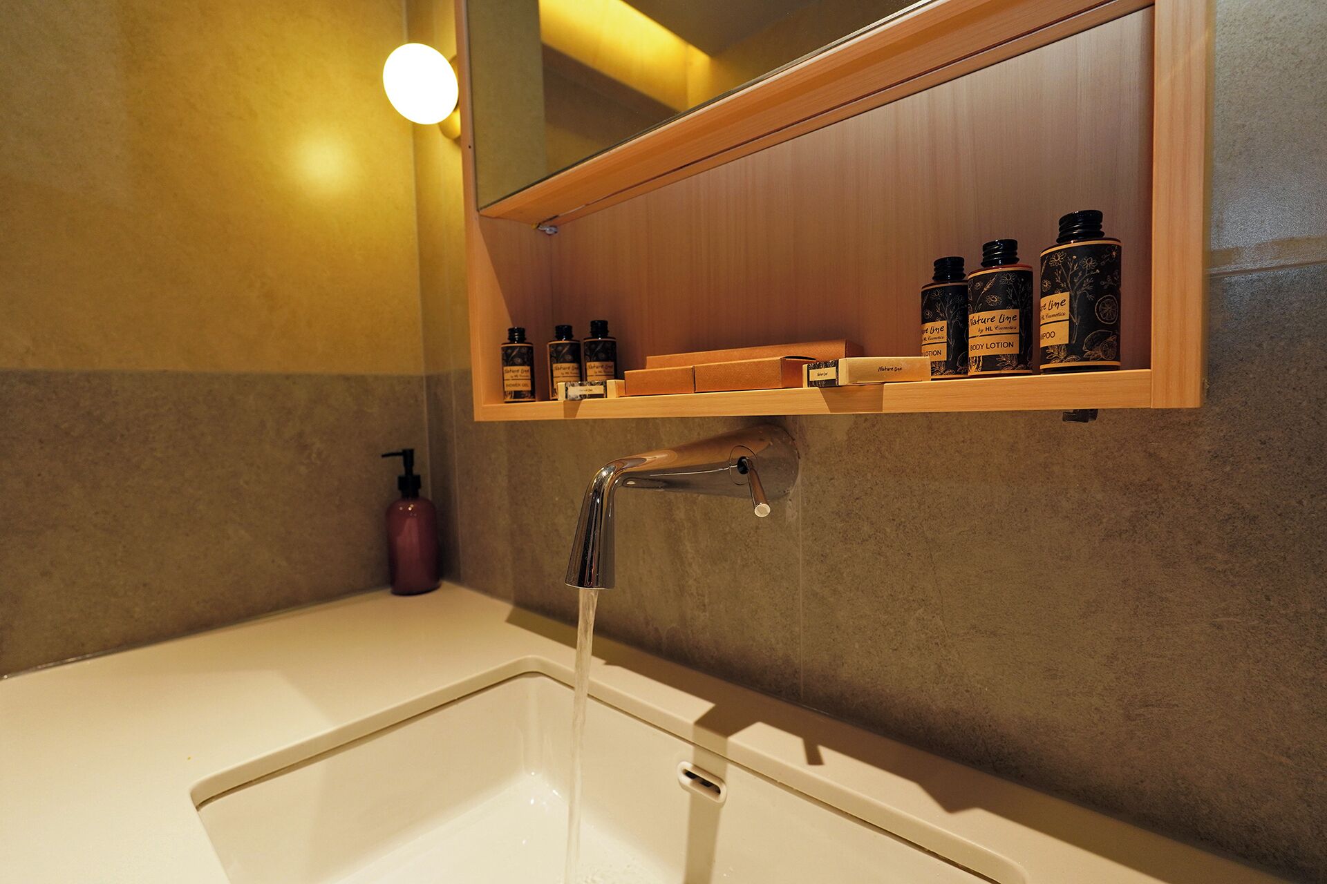 Une salle de bain avec un lavabo blanc, un miroir au-dessus et une étagère contenant des articles de toilette.