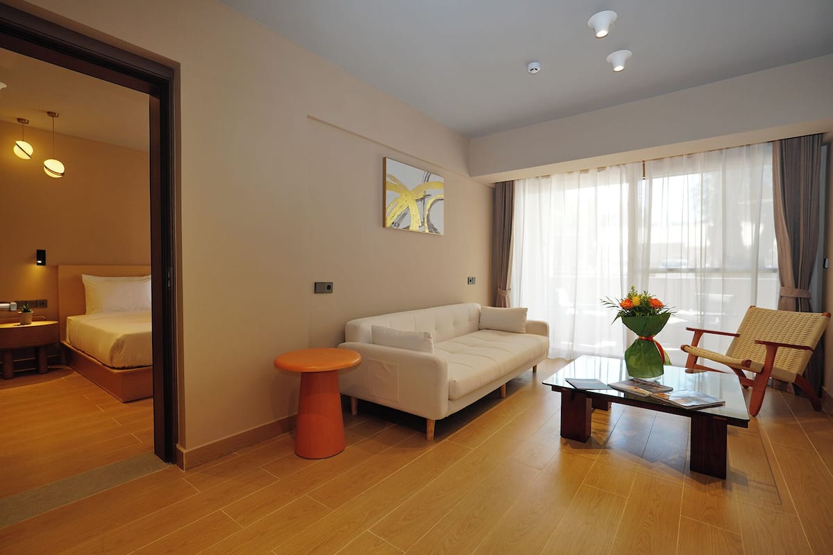 A modern hotel room with a sofa, a coffee table, a chair, and a bed.
