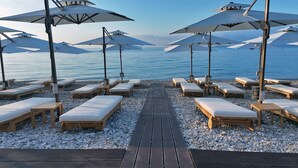 A beachside lounge area with sun loungers and umbrellas, a wooden deck, and a view of the sea. - Ionian Crown Suites in Barbati  (Corfu)