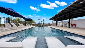 A swimming pool with lounge chairs, umbrellas, and a decorative fountain. - Vista Moon: Cabin D - Pool, Chapel, Fire Pit (Fredericksburg)