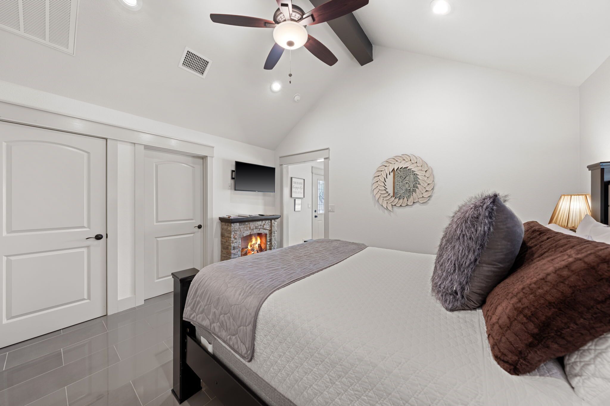 A bedroom with a bed, a fireplace, a ceiling fan, and white walls.