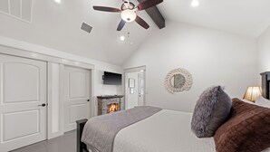 A bedroom with a bed, a fireplace, a ceiling fan, and white walls. - Vista Moon: Cabin D - Pool, Chapel, Fire Pit (Fredericksburg)