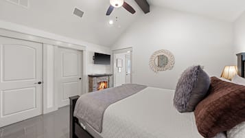 A bedroom with a bed, a fireplace, a ceiling fan, and white walls.