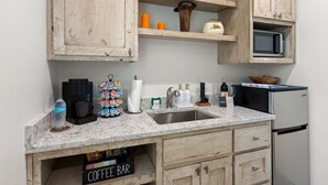 Una cocina con armarios de madera, encimera de mármol, cafetera, microondas y refrigerador.