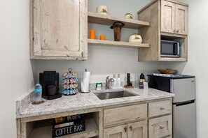 A kitchen with wooden cabinets, a marble countertop, a coffee maker, a microwave, and a refrigerator. - Vista Moon: Cabin H - Pool, Chapel, Fire Pit (Fredericksburg)