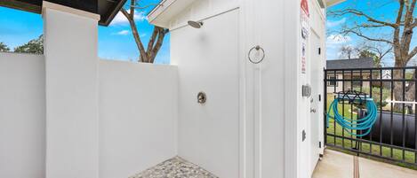 A white room with a shower, a door, a window, and a view of a tree and sky.