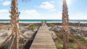 Une promenade en bois menant à la plage, bordée de palmiers.