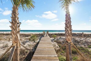 A wooden boardwalk leading to the beach, flanked by palm trees. - Page's Retreat|Gulf Front| Private Pool|Golf Cart (Panama City Beach)