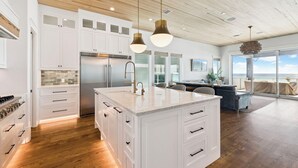 Une cuisine moderne avec des meubles blancs, un grand îlot central, des appareils en acier inoxydable et des luminaires suspendus.
