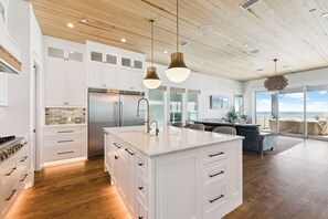 A modern kitchen with white cabinetry, a large island, stainless steel appliances, and pendant lighting. - Page's Retreat|Gulf Front| Private Pool|Golf Cart (Panama City Beach)
