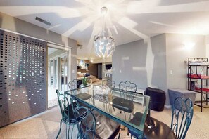 A modern dining area with a glass table and metal chairs, a decorative globe chandelier, and a perforated metal partition. - The Plantations condo with sunroom - near beach (Lewes)